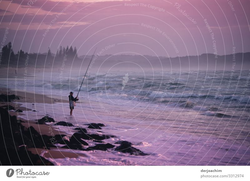 Very early in the morning while fishing at the sea. An angler stands on the beach, something in the water and has a fishing rod in his hand. Joy Relaxation