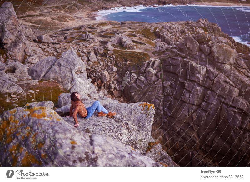 Woman sitting on a cliff near Baroña Castro in Galicia Barona celtic galicia spain hiking tourism nature coastline rocks landscape young woman one person beach