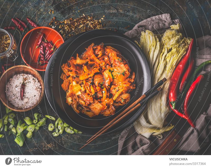 Homemade kimchi in black bowl on rustic background with ingredients: chinese cabbage , chili, spices and salt . Top view. Healthy fermented food homemade