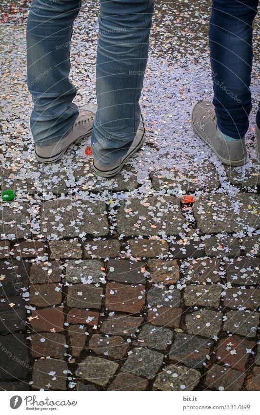 Three legs in jeans and sneakers, standing on the street in confetti, at carnival. Legs feet showery with confetti Confetti celebration celebrations Street