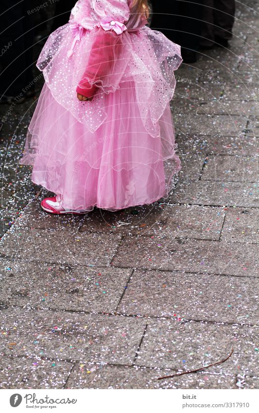 Little playful, dreamy, pretty, beautiful, sweet, dressed up princess in pink, pink dress with tulle, stands at carnival, carnival as a spectator, visitors at the carnival procession in the street, on confetti and looks, watches, enjoys the party.
