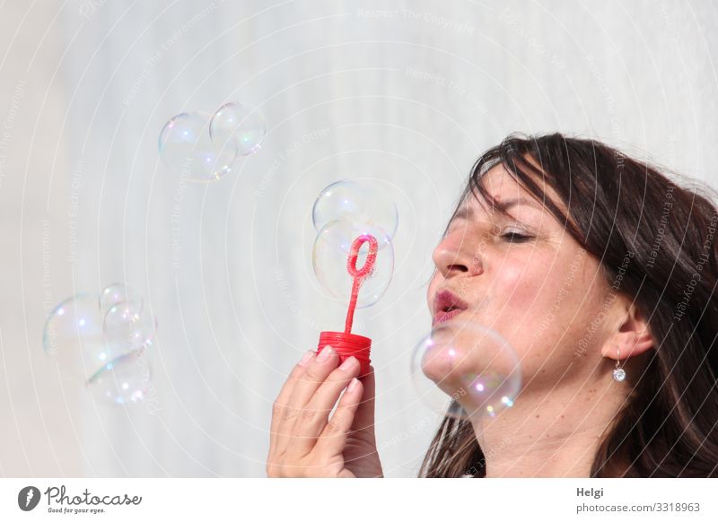 Face of a woman with brunette long hair blows soap bubbles Human being Feminine Woman Adults Head Hand 1 45 - 60 years Wall (barrier) Wall (building) Brunette