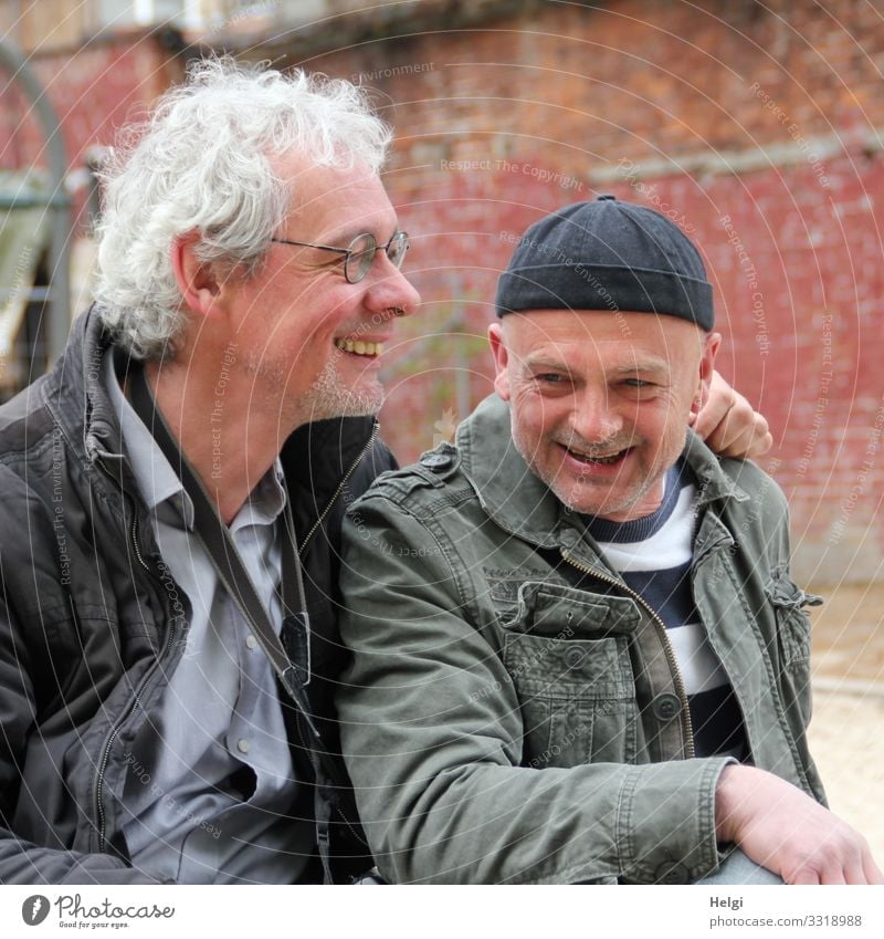 Portrait of two laughing seniors, one with silver-grey curls and glasses, the other with cap in front of an old wall Human being Masculine Man Adults