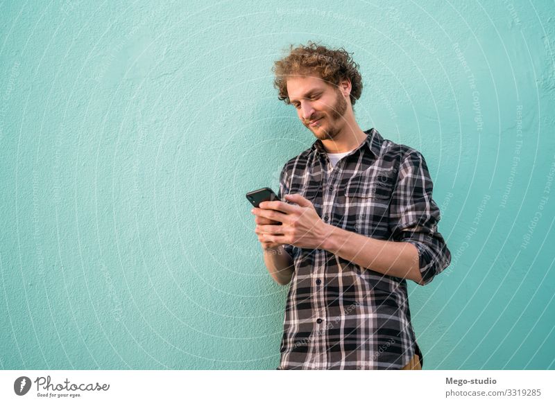 Portrait of young man using his mobile phone against blue background. Communication concept. Lifestyle Style Joy Happy Contentment Telephone PDA Technology