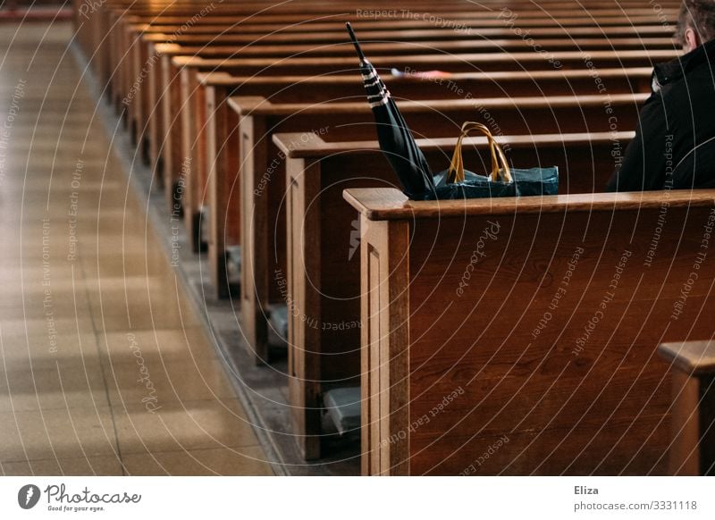 A man sits lonely and alone beside his umbrella and shopping bag on a pew in the church and prays Church Human being Church pew Sit Lonely by oneself Bench