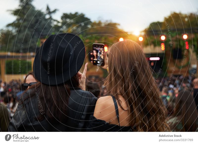 Long haired women taking selfies on smartphone standing in group pf people in sunny day friend photo festival celebration friendship communication together