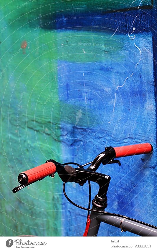 Bicycle handlebars from the bike, with red rubber grips, parked, in front of a blue, gaudy wall, during the break of the bike tour, in the city.