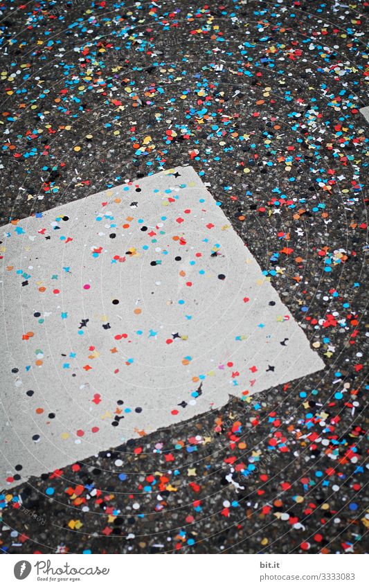 A lot of colorful confetti is spread out at carnival, carnival, fancy dress party, celebration on the gray ground of the street with markings and provides garbage and dirt.