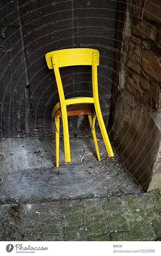 Bright, yellow, old, unused wooden chair, is leaning, tilted, against an old wooden door in an old, abandoned entrance of a stone house/barn. Furniture Chair