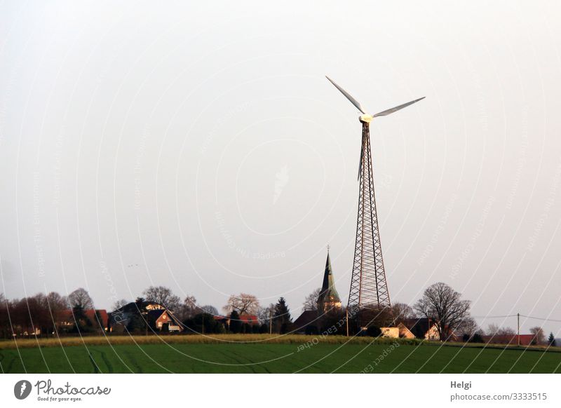 Windmill next to church tower in the village Technology Energy industry Renewable energy Wind energy plant Environment Nature Landscape Plant Winter Tree Grass