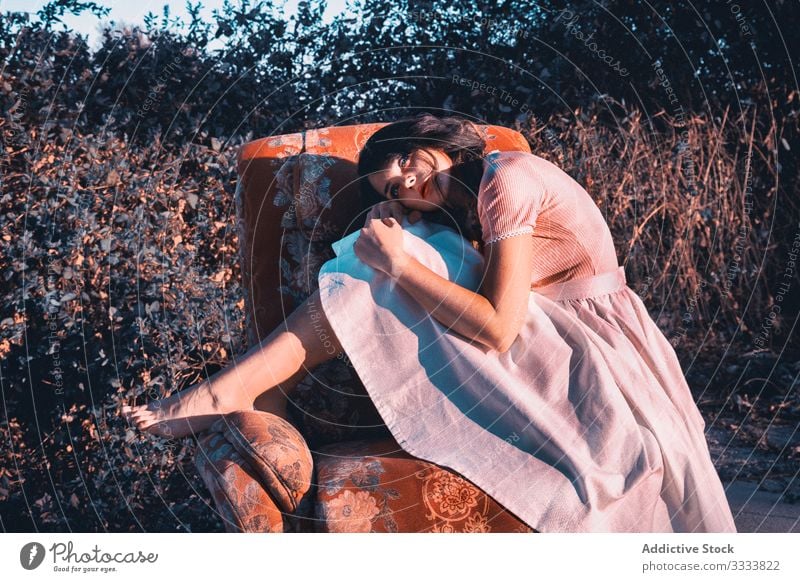 Dreamy female on armchair in countryside woman dreamy concept stylish comfort barefoot dress cute young nature bush shrub think ponder contemplate trendy