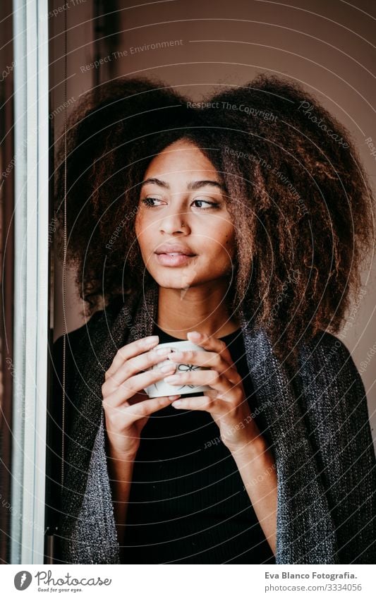 portrait of beautiful afro american young woman by the window holding a cup  of coffee. Lifestyle indoors - a Royalty Free Stock Photo from Photocase