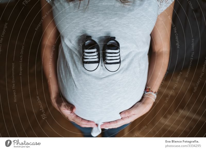 young pregnant woman at home holding baby shoes Pregnant Woman Home Bed pregnancy Baby expecting Showing one's bellybutton Day Lie tenderness pleasure