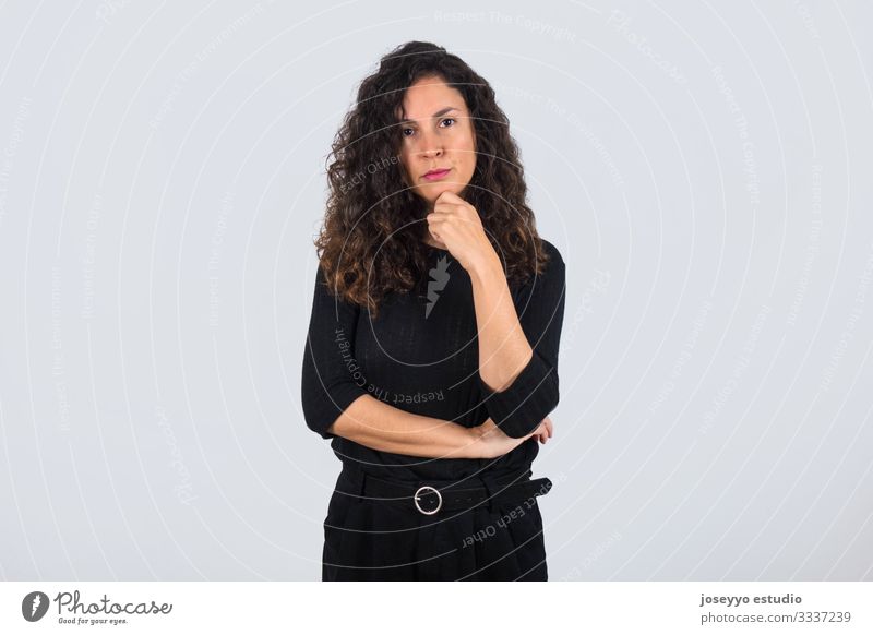 Curly Haired Brunette Woman Dressed In Black With Her Hand On Her Chin