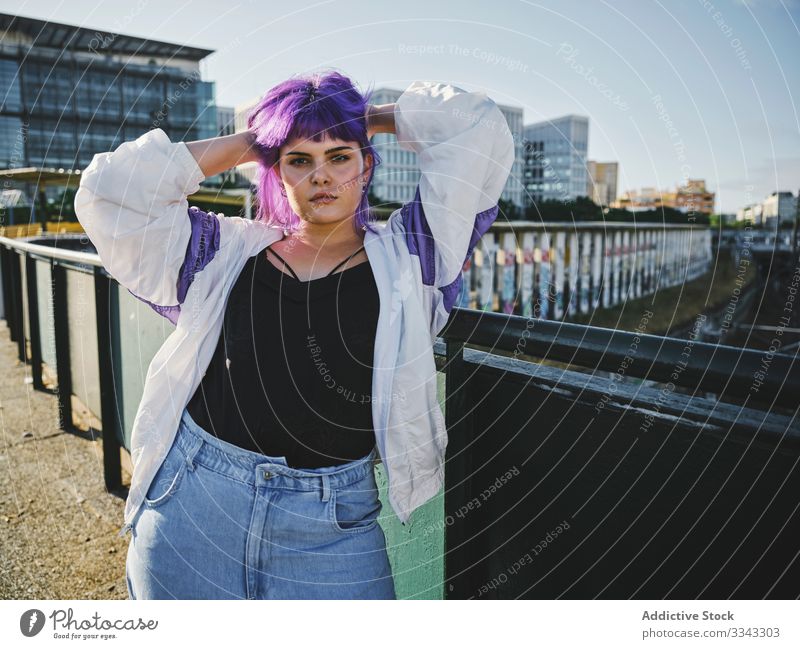 Woman with purple hair leaning on metal fence woman touching stylish urban hairstyle jacket shiny district confident fashion young model street human female