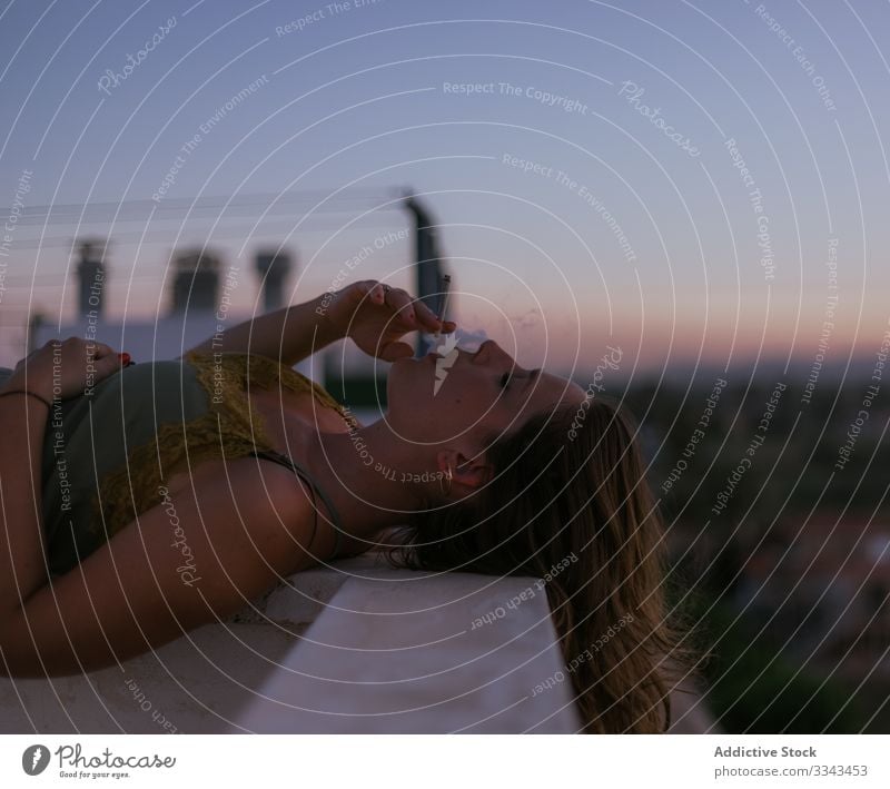 Serene woman having relaxation with cigarette on balcony smoking closed eyes lying resting fence terrace sunset evening nature sky heaven female lady lifestyle