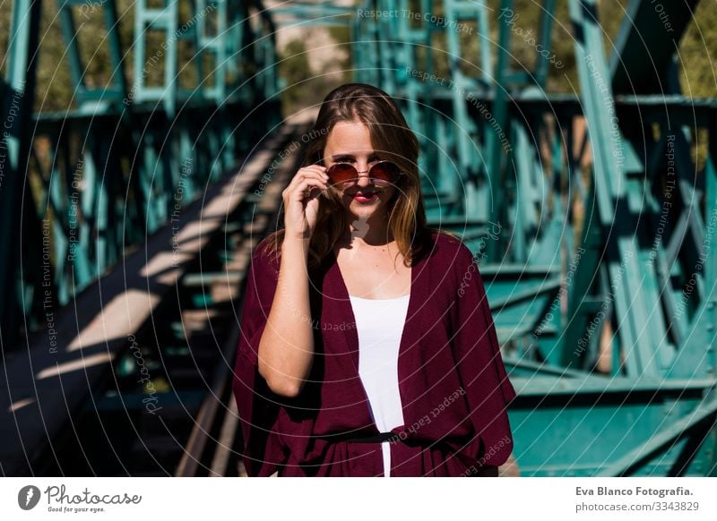 portrait of a young beautiful woman on a green bridge. Wearing stylish clothes. Holding sunglasses. LIfestyle. Outdoors. Sunny Railroad Woman pretty