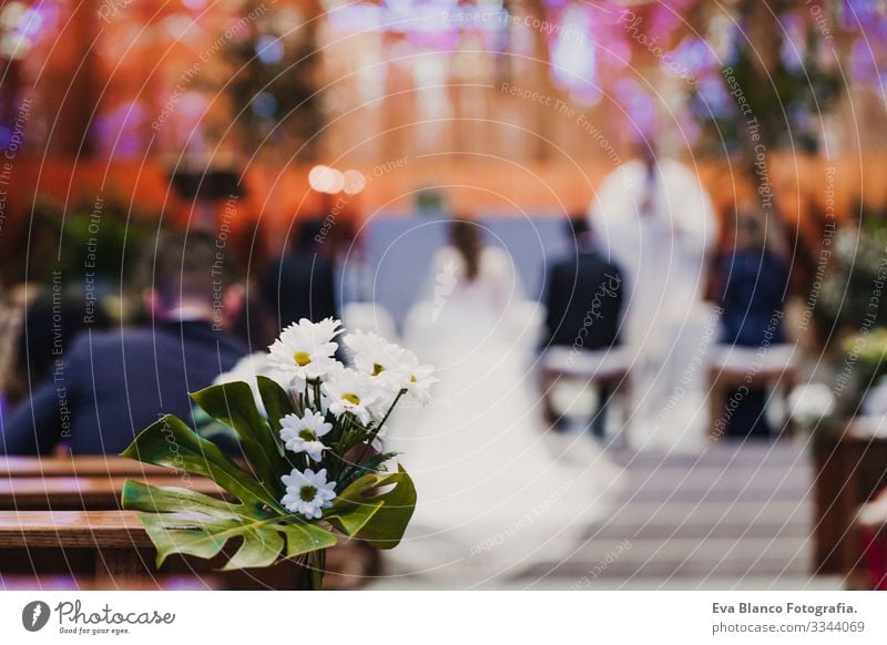 Beautiful flower wedding decoration in a church. Selective focus. Unrecognizable blurred Groom and bride on background. Marriage concept in church bunch White