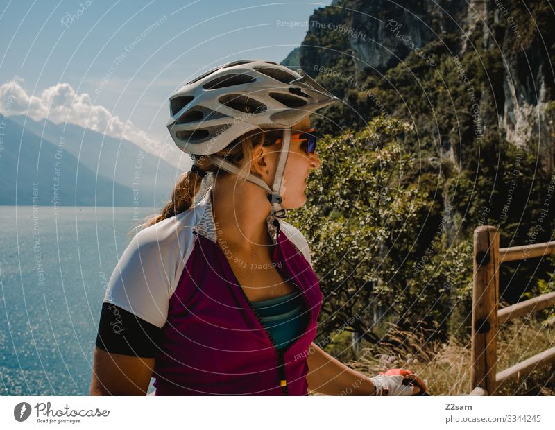 Mountain biker at Lake Garda alpine crossing mtb transalp panorama Sportsperson Athletic Braids Blonde Helmet Safety Protection Vantage point cliffs ponal