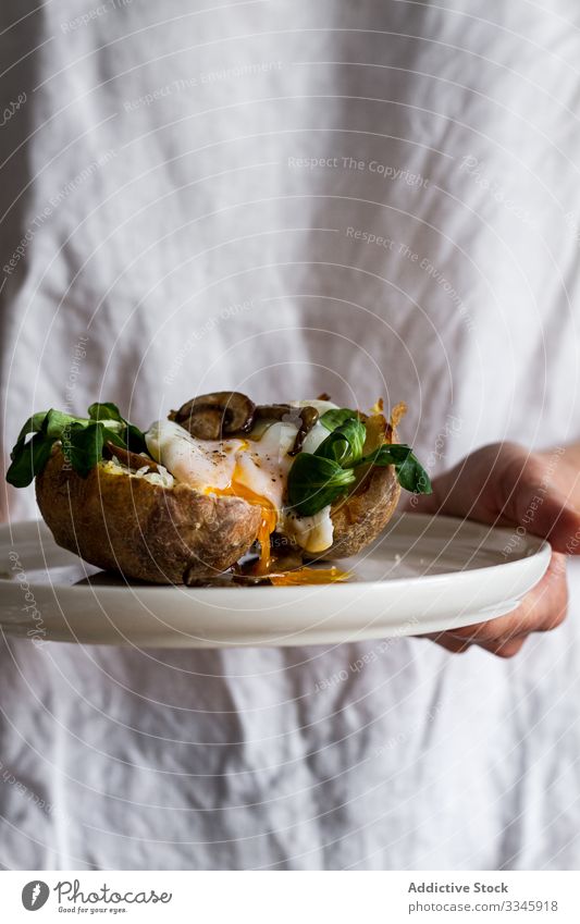 Hand with delicious dish of potato with eggs stuffed potatoes filled hand arm fried mushroom herb green rustic table wooden homemade towel food traditional