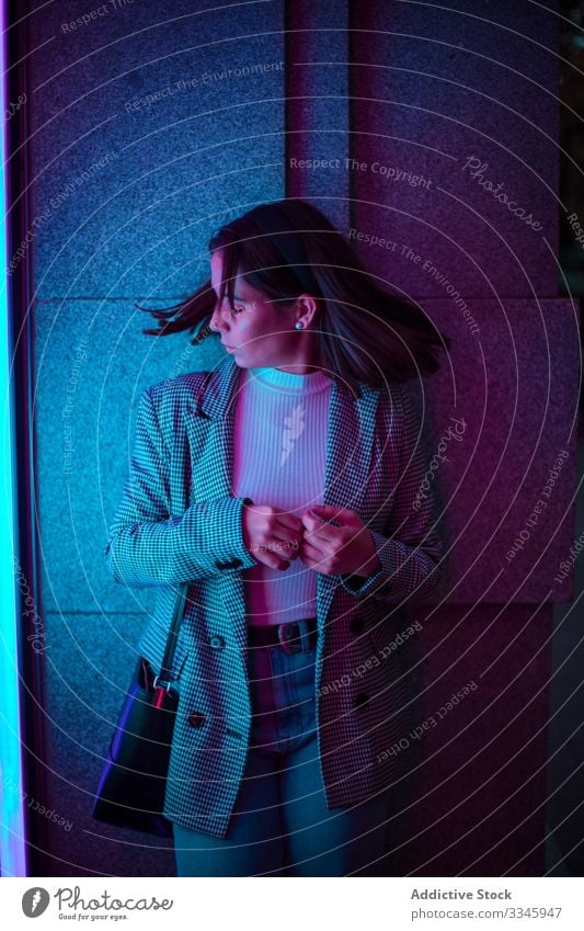 Young woman in casual outfit in neon light style clothing standing shaking head hair waving fashionable hipster millennial teenager city street urban lifestyle