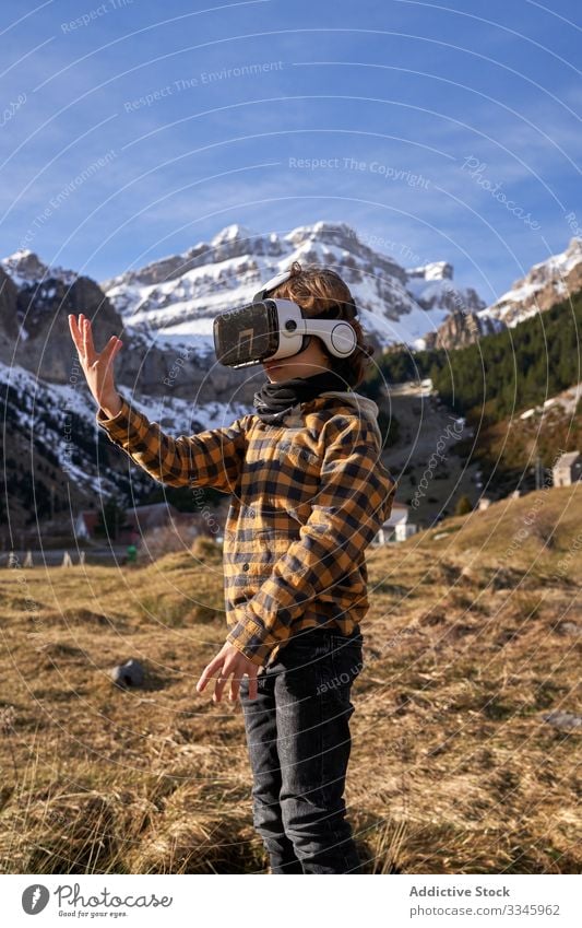 Boy standing on stone in VR glasses against mountain boy vr nature valley virtual reality headset modern device entertainment explore terrain technology digital