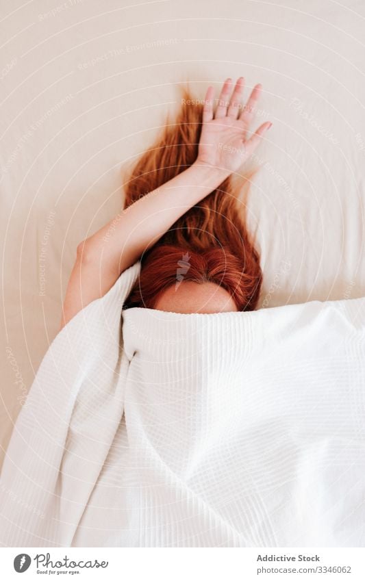 Lazy morning of anonymous sleepy woman lying bed hiding arm hand blanket cover under relax rest redhead lifestyle lady female home comfortable lazy pillow