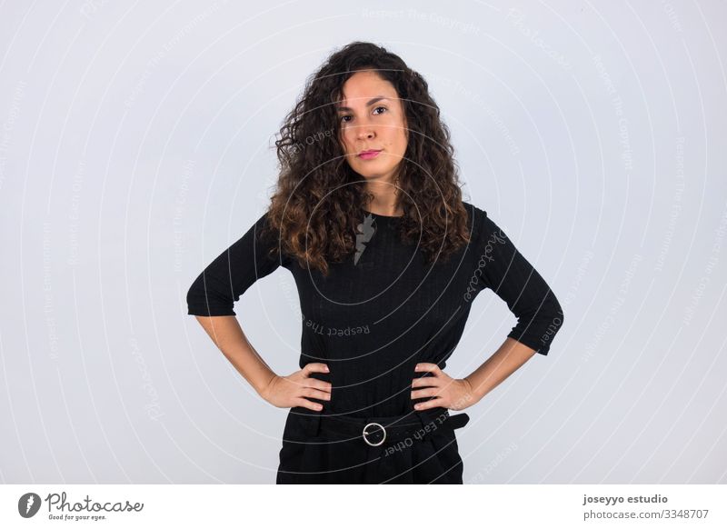 Curly haired brunette woman dressed in black with her hands on her waist looking at camera. 30-40 years advertisement attitude background beauty brown casual