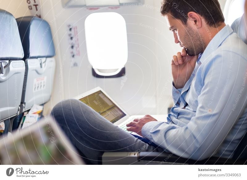 Casually dressed middle aged man working on laptop in aircraft cabin during his business travel. Shallow depth of field photo with focus on businessman eye.