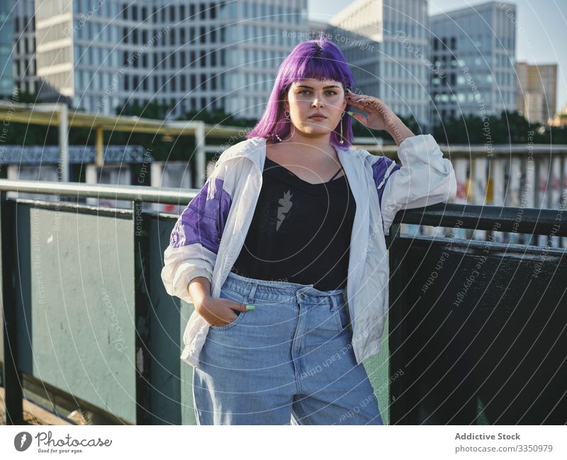 Woman with purple hair leaning on metal fence woman touching stylish urban hairstyle jacket shiny district confident fashion young model street human female