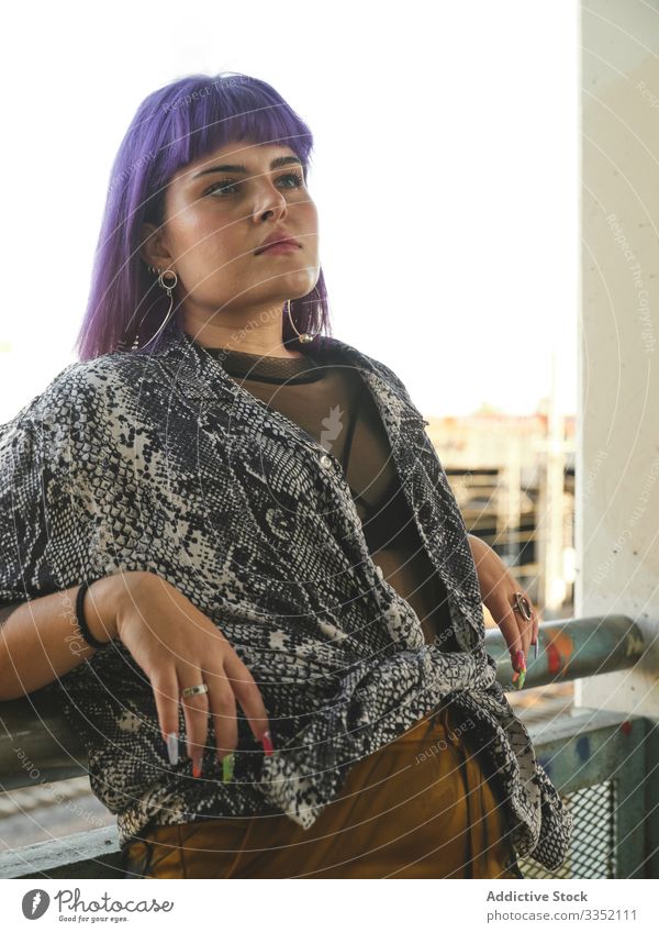 Woman with purple hair leaning on metal fence and looking away woman stylish urban hairstyle construction shiny structure district confident fashion young model