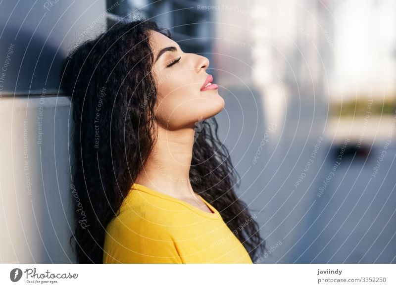 Young Arab woman with her eyes closed and her head leaning against the wall in the street. Lifestyle Style Beautiful Hair and hairstyles Make-up Sun Human being