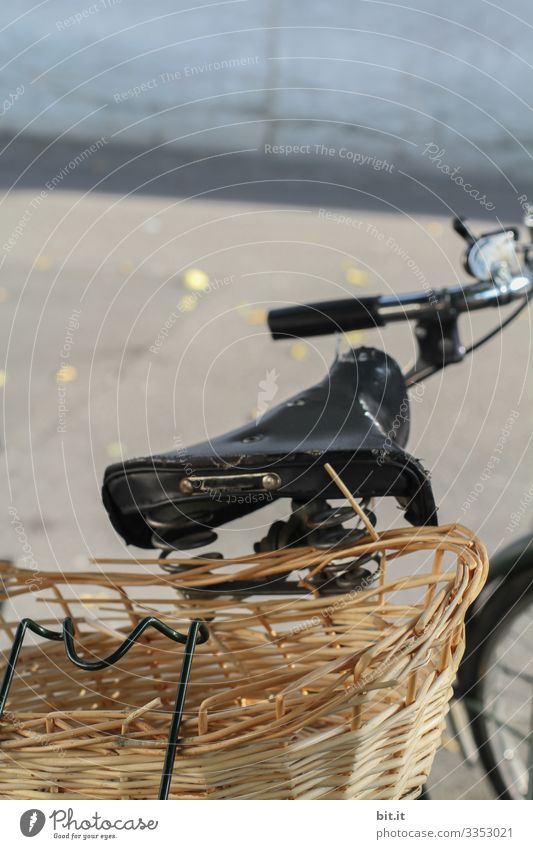 Old bicycle with handlebars, saddle and basket for shopping and transport stretched on the luggage rack, parked on the street, in the city, in front of a grey wall in the background. The bike basket is brown, broken, old, practical and beautifully exposed.