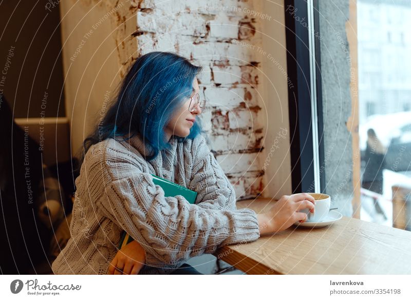 Young adult female with dyed blue hair drinking coffee in a coffeeshop during blue hour, shallow selective focus Asians Cozy Evening Reading Sweater