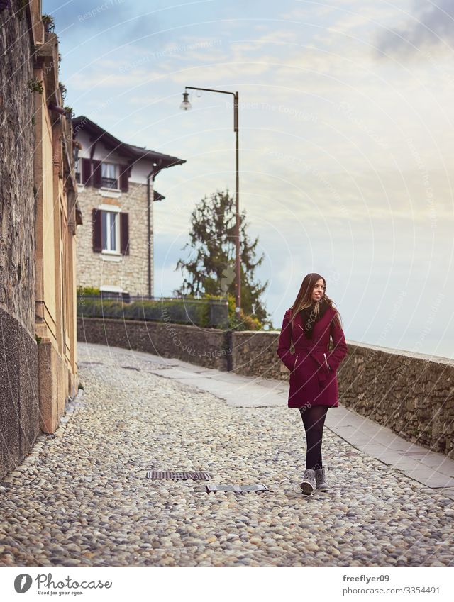 Young woman walking by a pedestrian street in italy red coat young blonde sky hiking tourism europe european trip holiday discover sightseeing vacation relaxing