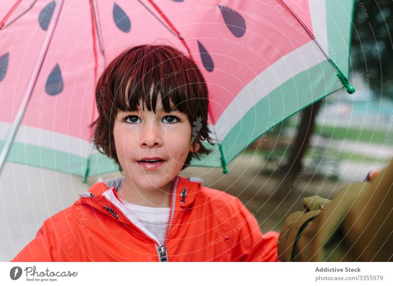 Cute child with colorful umbrella looking at camera in park alley rain season funny water wet dirt childhood mud autumn game active weather rubber boots