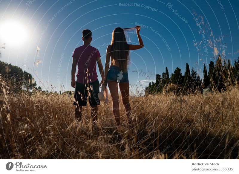 Playful young male standing with female in field with hat in hand friend play nature travel adventure activity together playful sky freedom journey relax