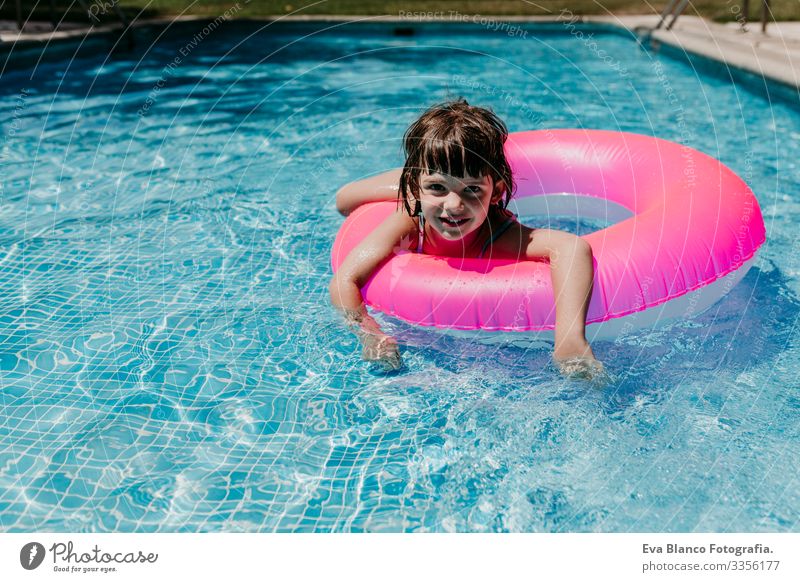 beautiful kid girl floating on pink donuts in a pool. Wearing sunglasses and smiling. Fun and summer lifestyle Action Swimming pool Beauty Photography