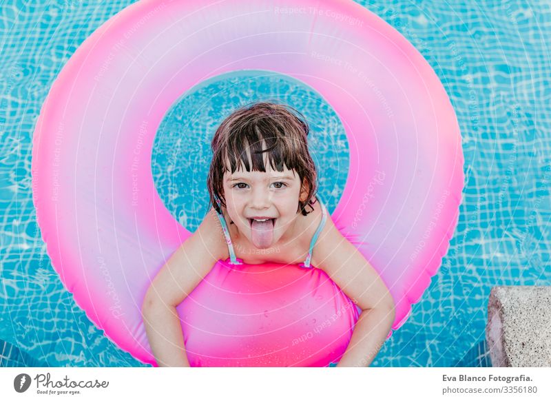 beautiful kid girl floating on pink donuts in a pool. Smiling. Fun and summer lifestyle Action Swimming pool Beauty Photography Exterior shot