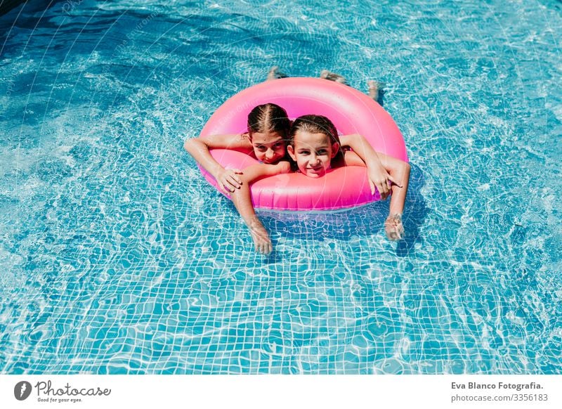 two beautiful teenager girls floating on pink donuts in a pool. smiling. Fun and summer lifestyle Action Swimming pool Exterior shot Youth (Young adults) Girl