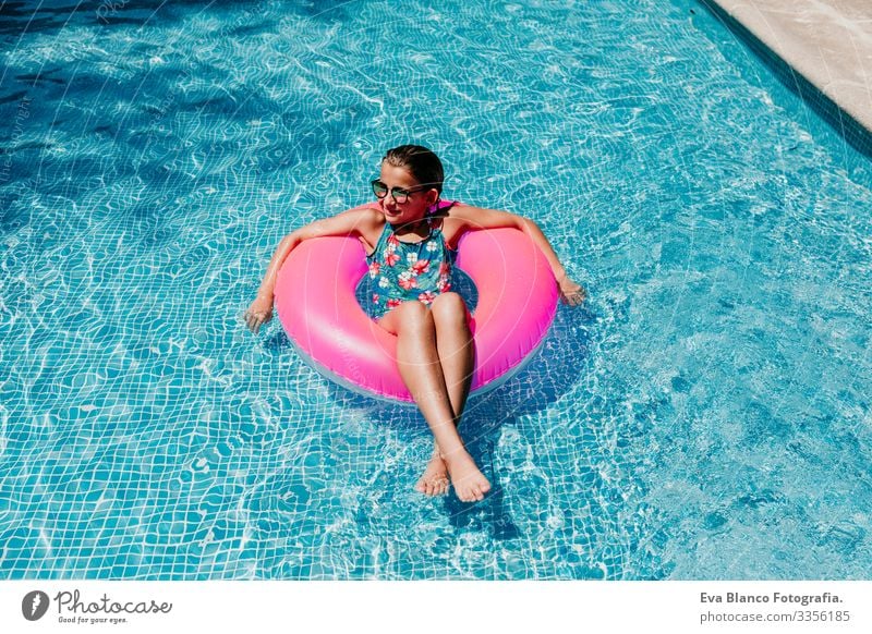 beautiful teenager girl floating on pink donuts in a pool. Wearing sunglasses and smiling. Fun and summer lifestyle Action Swimming pool Beauty Photography