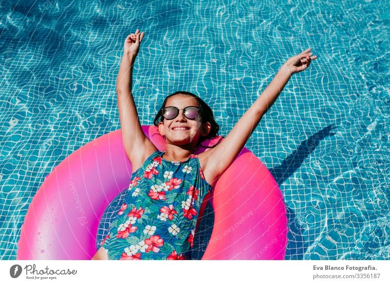 beautiful teenager girl floating on pink donuts in a pool. Wearing sunglasses and smiling. Fun and summer lifestyle Action Swimming pool Beauty Photography