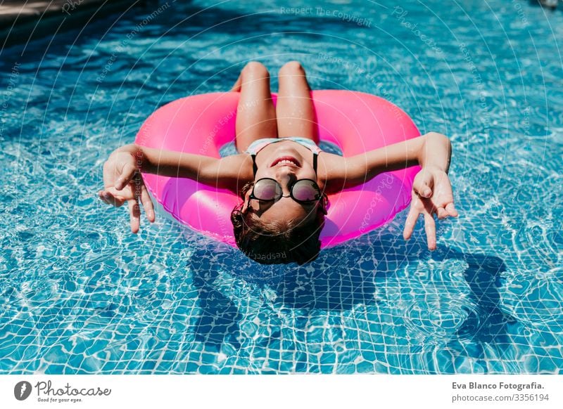 beautiful teenager girl floating on pink donuts in a pool. Wearing sunglasses and smiling. Fun and summer lifestyle Action Swimming pool Beauty Photography