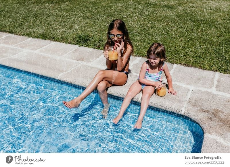 two beautiful sisters at the pool drinking orange juice, summer time Child Family & Relations two sisters Friendship Together To enjoy Floating Donut Caucasian