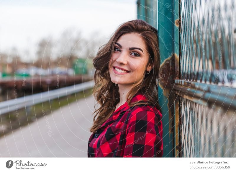 young beautiful woman standing by a fence. she is wearing casual clothes and smiling. Outdoors city background. Lifestyle Town Hat Beautiful Stand Attractive
