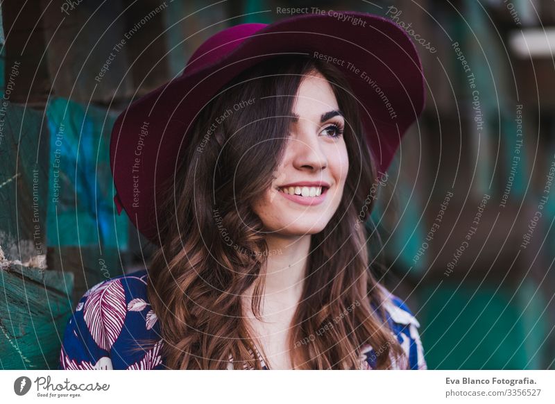 portrait of a young beautiful woman wearing casual clothes and a modern hat, standing over green wood blocks background and smiling. Outdoors lifestyle.