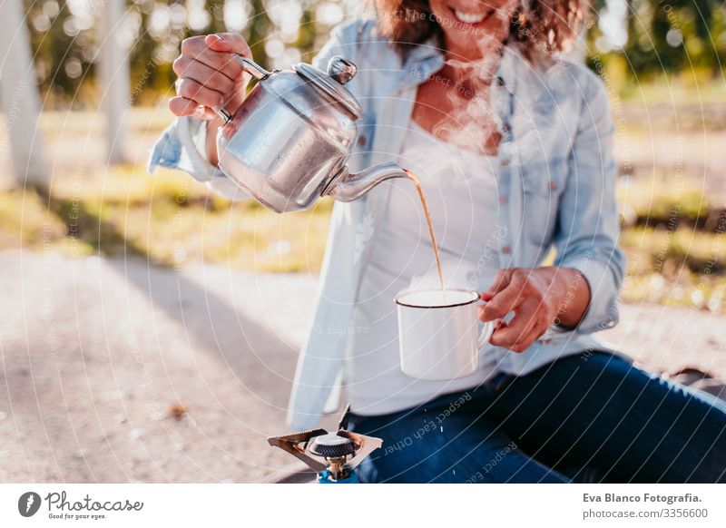 young woman pouring tea with pot outdoors. Using stove. camping concept Youth (Young adults) Woman Camping Pot Stove & Oven Sunset preparing Hot Tea Teapot