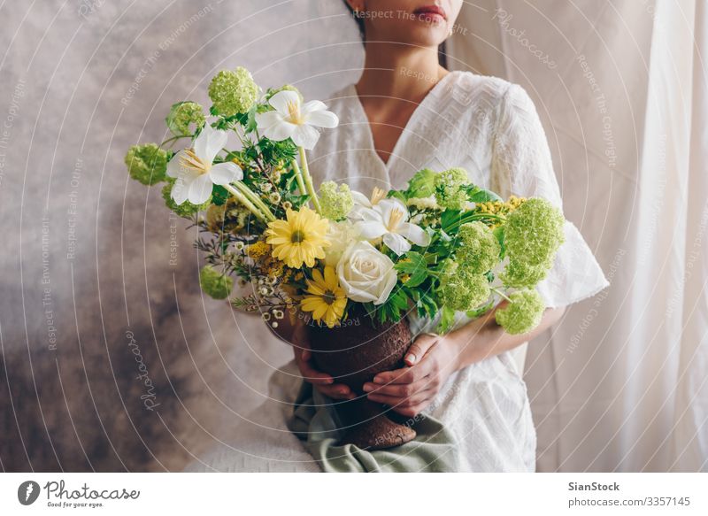 Young woman in a white dress holding vase with flowers. Lifestyle Elegant Style Happy Beautiful Chair Wedding Woman Adults Lips Hand Flower Dress Brunette