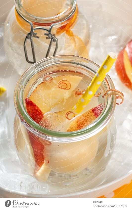 Cool lemonade with juicy nectarine in glass and yellow drinking straw on a white tray full of ice cubes Cold drink Fruit Nectarine Beverage Ice cube Vitamin