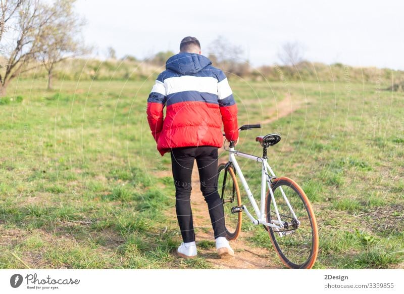 Rear view of a young man walking on a park with a fixed bike Lifestyle Style Happy Leisure and hobbies Music Telephone Cellphone PDA Technology Human being